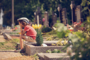 Sad little boy sitting on a grave in a cemetery feeling sad and crying